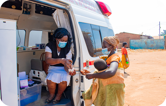 A Wandikweza health worker assisting a mother and child at a mobile clinic van